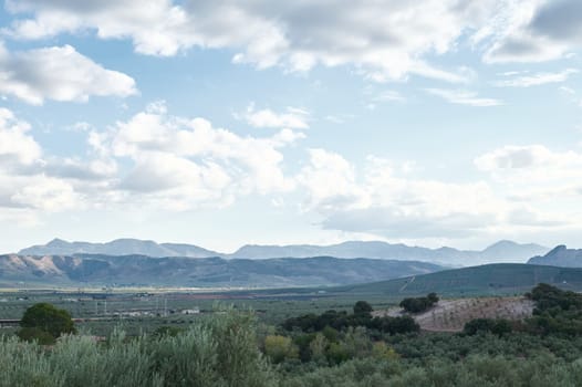 Breathtaking view of a mountainous landscape under a partially cloudy sky, with rolling hills and lush vegetation in the foreground.