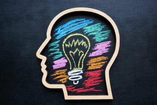 Outline of a head with light bulb drawn in chalk. Creative thinking skills and development.