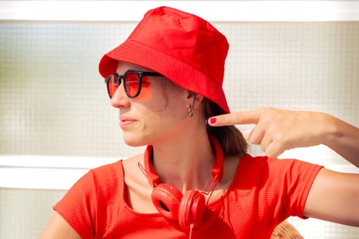 A young Caucasian woman with a hat and red headphones is sitting pointing with her thumb to the left side, with an angry face. outside