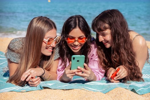 Three young women using apps on their cell phones on the beach