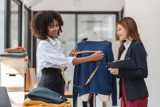 Two female designers working together in a modern studio, measuring and designing a shirt on a mannequin.