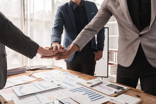 A business team working together, expressing opinions, and collaborating on work with documents and charts spread out on the table in a modern office setting.