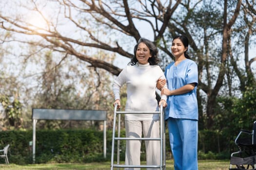 Elderly woman using a walker with the help of a caregiver in a park, focusing on rehabilitation and support.