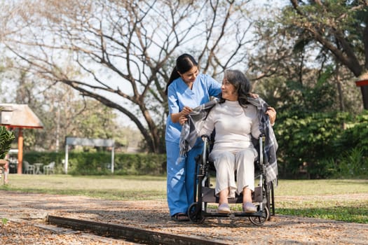 Caregiver helping an elderly woman in a wheelchair during a rehabilitation session outdoors in a park, promoting health and well-being.