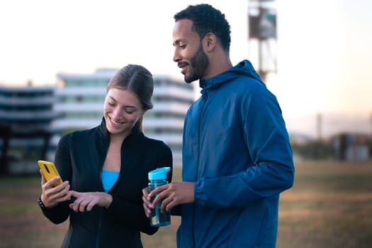 Young couple using a social media app on smartphone while exercising outdoors.