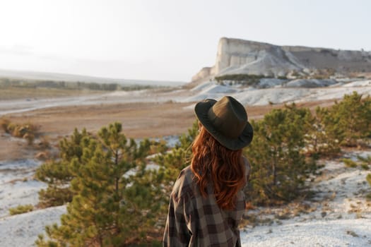 Woman in plaid shirt and hat gazing at majestic mountain range in awe