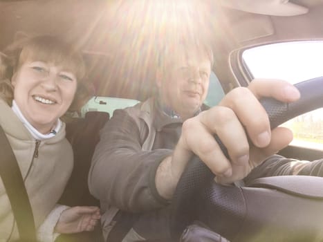 An elderly couple is happily driving through sunny countryside, enjoying their daytime road trip together