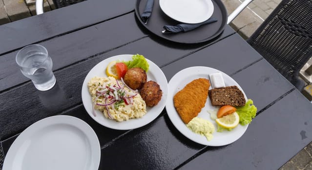 Seafood restaurant on the seashore. White plate with fish patties, fish fillets and potato salad. High quality photo