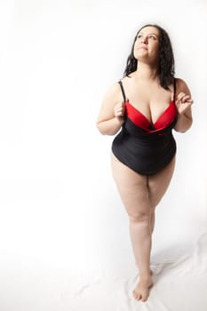 Portrait of attractive dreamy thick woman in red black swimsuit posing on white background. Body positive, photoshoot, selfie. Funny plus size model