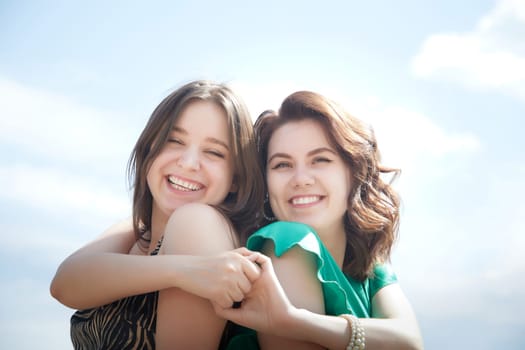 Happy Girls Enjoying Summer Day Together in the Park. Two young women stand on a platform in a park under a bright summer sky, smiling and relaxed