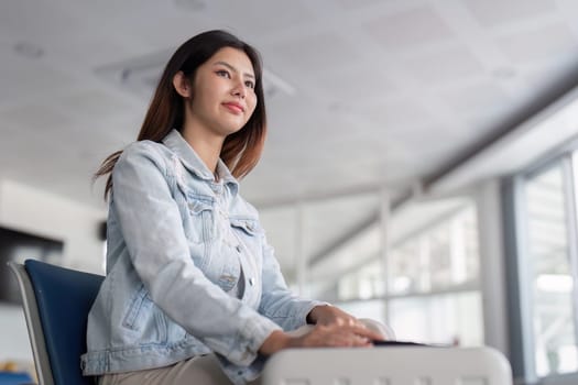 A young female tourist sits in a modern airport terminal, waiting for her flight. The terminal features natural light and contemporary design elements.