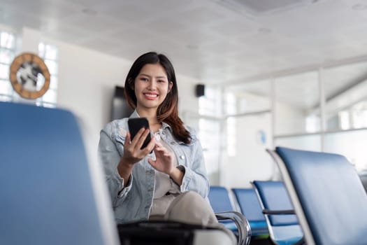 A cheerful tourist sits in a modern airport terminal, using a smartphone while waiting for their flight.