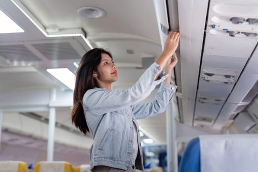 A young female tourist places her luggage in the overhead compartment of an airplane, preparing for travel. The airplane interior is modern and well-lit.