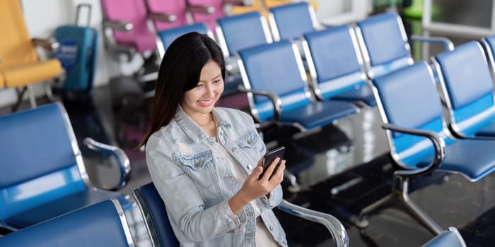 A cheerful tourist using a smartphone while waiting in a modern airport terminal with colorful seating. Ideal for travel, technology, and lifestyle themes.