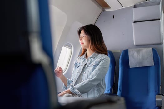 A young tourist woman sits comfortably in an airplane seat, gazing out the window, enjoying her travel experience on a modern aircraft.