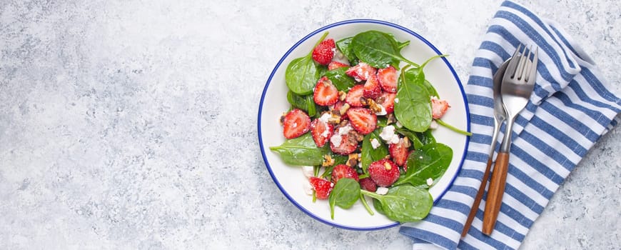 Light Healthy Summer Salad with fresh Strawberries, Spinach, Cream Cheese and Walnuts on White Ceramic Plate, white rustic stone Background From Above, Space For Text.