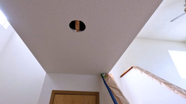 View of a ceiling with a circular cutout, ready for the installation of a new light fixture. The room is brightly lit with natural light from skylights, showcasing the ongoing home improvement project.