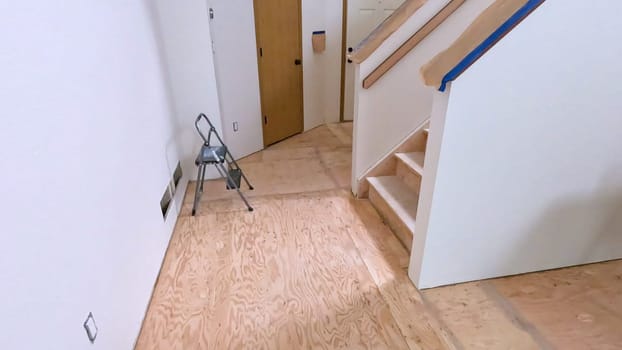 A staircase in a home undergoing renovation, featuring protective coverings and masking tape to safeguard surfaces. The area is prepared for painting or further construction work, highlighting a common home improvement project.