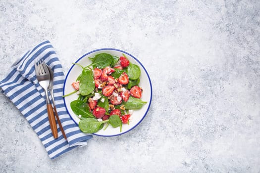 Light Healthy Summer Salad with fresh Strawberries, Spinach, Cream Cheese and Walnuts on White Ceramic Plate, white rustic stone Background From Above, Space For Text.