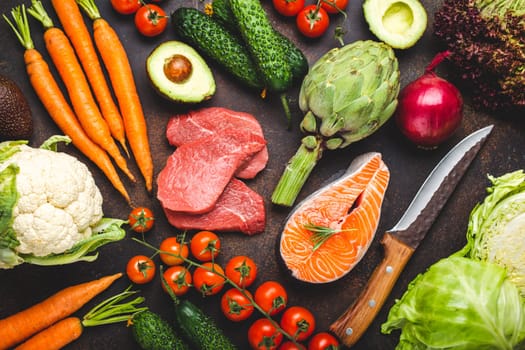 Assorted food raw products: vegetables, beef meat, fish salmon and knife on dark rustic brown stone table top view. Healthy food background, ingredients with vitamins concept, cooking and nutrition