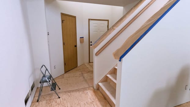 A staircase in a home undergoing renovation, featuring protective coverings and masking tape to safeguard surfaces. The area is prepared for painting or further construction work, highlighting a common home improvement project.