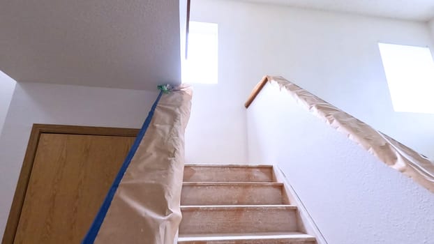 A staircase in a home undergoing renovation, featuring protective coverings and masking tape to safeguard surfaces. The area is prepared for painting or further construction work, highlighting a common home improvement project.