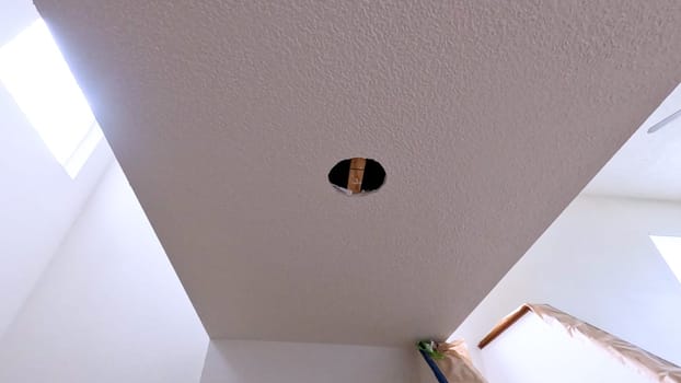 View of a ceiling with a circular cutout, ready for the installation of a new light fixture. The room is brightly lit with natural light from skylights, showcasing the ongoing home improvement project.