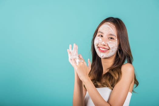 Portrait Asian young woman hands are adorned with white foam cleaning face studio shot isolated on blue background, beautiful female holds a cleansing foam on palm, Cosmetics beauty skincare