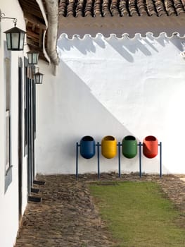 A tidy row of blue, yellow, green, and red waste bins lines a traditional cobbled street.