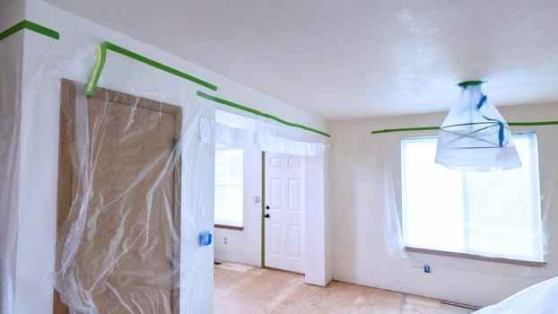 An interior home renovation scene showing rooms prepped with plastic coverings and masking tape. The space is ready for painting or further construction, highlighting the careful preparation steps in home improvement projects.