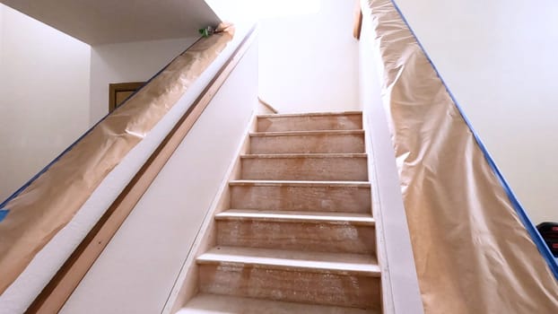 A staircase in a home undergoing renovation, featuring protective coverings and masking tape to safeguard surfaces. The area is prepared for painting or further construction work, highlighting a common home improvement project.