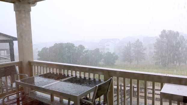 Image capturing a hail storm on a wooden deck, highlighting the impact of hail on patio furniture and the deck surface. Hailstones are visible scattered across the wet deck, with patio furniture in the background.