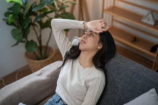 A young woman experiencing a headache and migraine, feeling sick and unwell, resting on a couch at home, holding her forehead in discomfort.