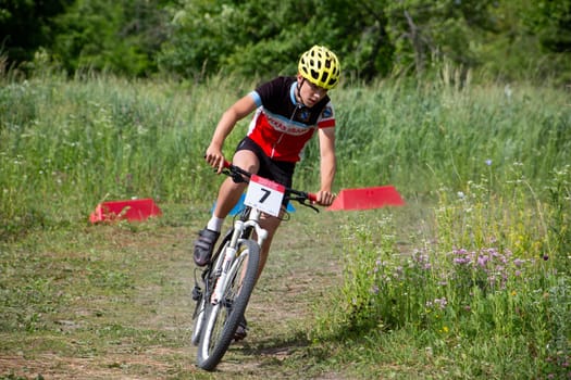 Kursk, Russia, June 15, 2024: Young cyclist at mountain bike competition takes turn on the grass on sunny day