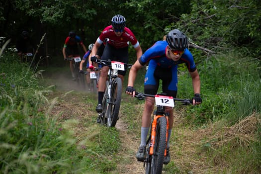 Kursk, Russia, June 15, 2024: Young cyclists overcome obstacles over hills on mountain bikes, cross country cycling competition