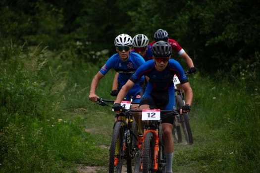 Kursk, Russia, June 15, 2024: Row of athletes at off-road cycling competition fight for position, line of mountain bike racers in forest