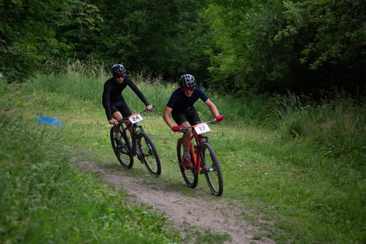 Kursk, Russia, June 15, 2024: Two athletes on bicycles fight for position on path in forest, off road cycling competition