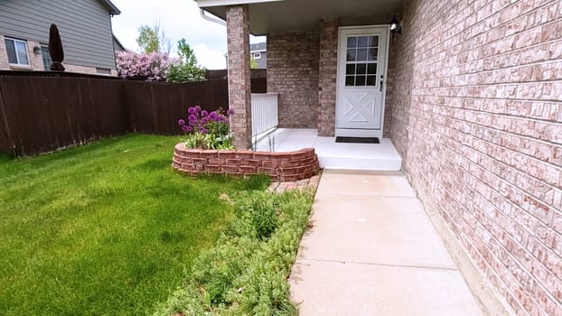 The front porch of a charming brick house featuring a white door and a well-maintained garden bed with blooming purple flowers. The neatly trimmed lawn and inviting entryway enhance the home curb appeal.