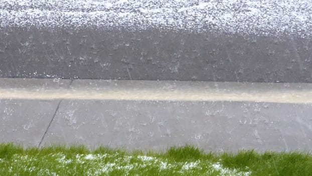 A lawn and rock garden blanketed in hail following a storm, with the green grass and small shrubs peeking through the layer of ice. The contrast between the white hail and the greenery creates a striking visual effect.