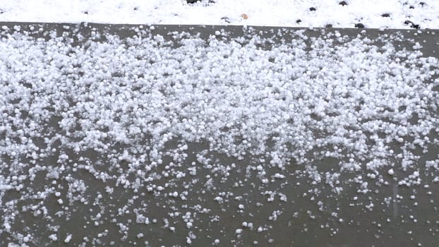 A detailed image showing a close-up view of hailstones densely covering an outdoor surface. The hailstones create a thick layer, illustrating the intensity of the hail storm.