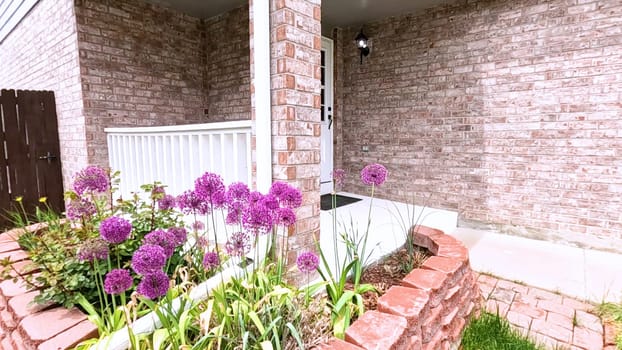 The front porch of a charming brick house featuring a white door and a well-maintained garden bed with blooming purple flowers. The neatly trimmed lawn and inviting entryway enhance the home curb appeal.