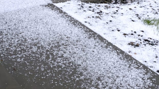 A lawn and rock garden blanketed in hail following a storm, with the green grass and small shrubs peeking through the layer of ice. The contrast between the white hail and the greenery creates a striking visual effect.