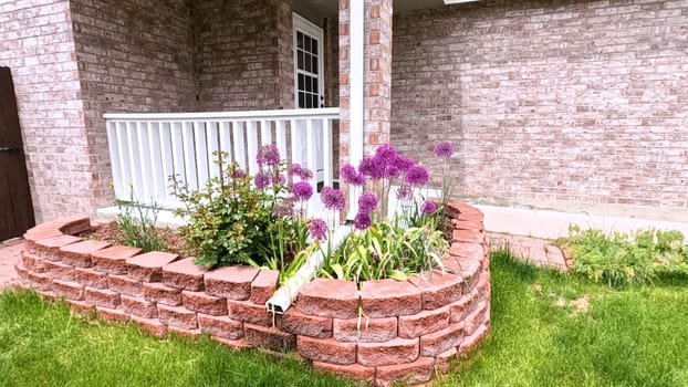 The front porch of a charming brick house featuring a white door and a well-maintained garden bed with blooming purple flowers. The neatly trimmed lawn and inviting entryway enhance the home curb appeal.
