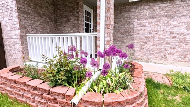 The front porch of a charming brick house featuring a white door and a well-maintained garden bed with blooming purple flowers. The neatly trimmed lawn and inviting entryway enhance the home curb appeal.