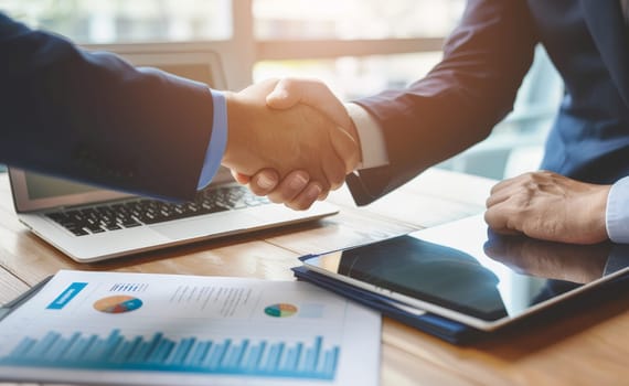 Two men shaking hands in front of a laptop and a tablet by AI generated image.