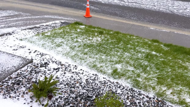 A lawn and rock garden blanketed in hail following a storm, with the green grass and small shrubs peeking through the layer of ice. The contrast between the white hail and the greenery creates a striking visual effect.