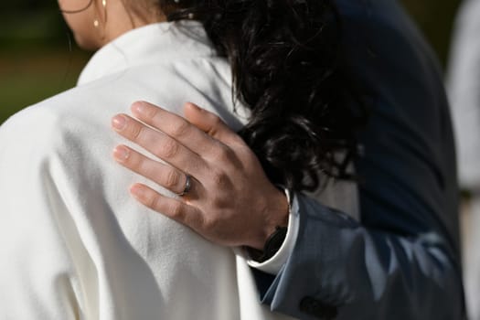 The groom hugs the bride by the shoulder with his hand, which is wearing a ring