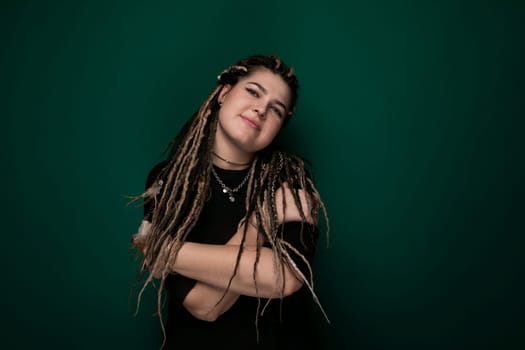 A woman with dreadlocks standing confidently in front of a bright green background. Her distinctive hairstyle stands out against the vibrant backdrop.