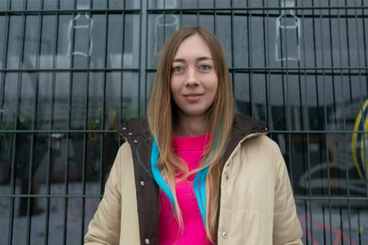 A middle-aged woman is standing in front of a wooden fence, looking straight ahead. She is wearing casual clothing and appears to be deep in thought in a rural setting.