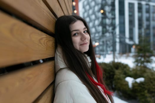 A woman leaning against a wooden bench covered in snow. The snow-covered ground and bench contrast with the dark clothing worn by the woman. She appears to be looking off into the distance.
